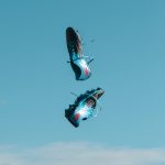 pair of blue-and-black New Balance cleats in the air under teal sky with white clouds